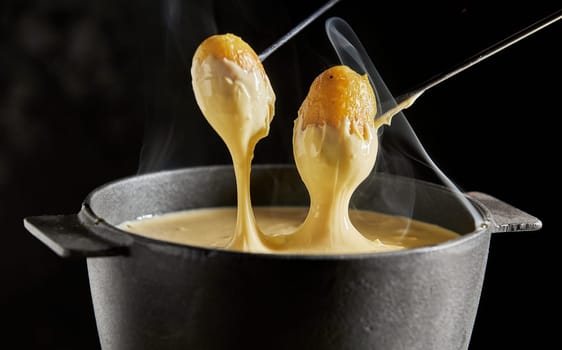 Delicious hot steaming Swiss cheese fondue served with grilled baby potatoes for dipping in close up over a dark background