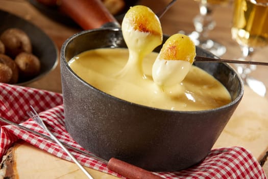 Dipping grilled baby potatoes into a traditional hot steaming melted cheese fondue served with wine for a tasty Swiss meal