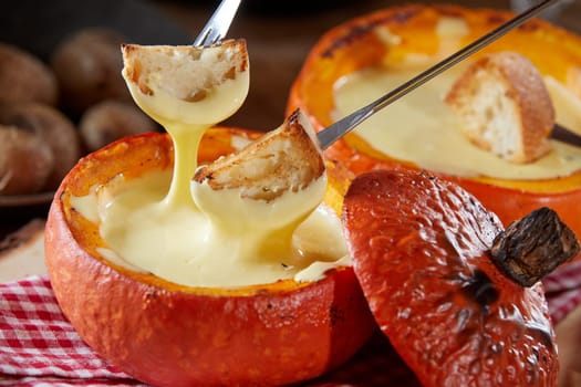 Delicious raclette melted cheese fondue served in a hollowed pumpkin with toasted baguette dipping pieces on forks in close up for a tasty fall meal