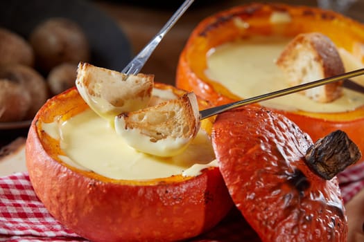 Traditional Swiss fondue with melted raclette cheese served in a hollow roasted pumpkin with toasted baguette for dipping, in close up
