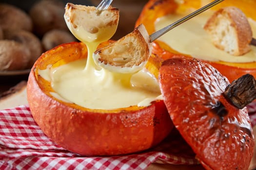 Tasty cheese fondue served in a colorful orange pumpkin rind in autumn in close up with forks dipping toasted baguette