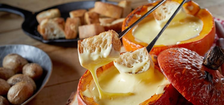 Panorama banner eating a traditional cheese fondue with toasted baguette and baked baby potatoes on forks for dipping in close up