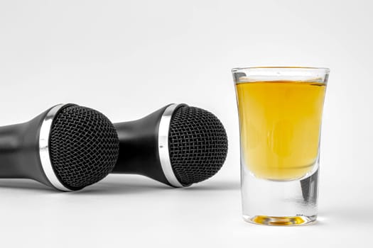 A shoot glass with liquor and two karaoke microphones on a white background