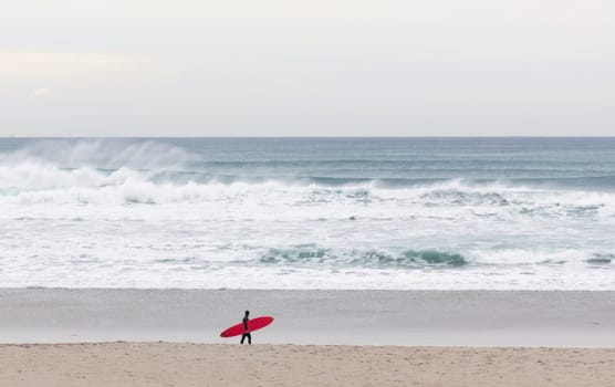 Red board surfer walking on the beach with waves in the background