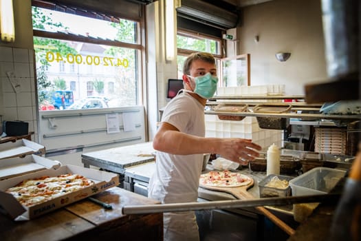 Man is working in a pizza restaurant drive with his mask and covid 19 protection. Pandemic situation