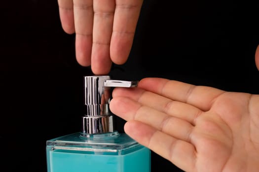 Close up of a person getting soap from a soap dispenser on a black background