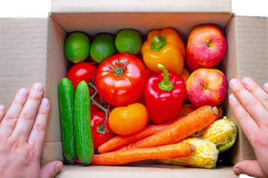 A person opening a deliver cardboard box with produce, fruits and vegetables inside on a white background