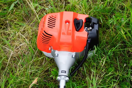 The engine of a gas trimmer lies on the grass. Power part of the trimmer. Trimer gascosis with a leaf for mowing grass and shrubs.
