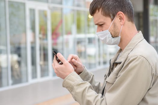 A man in a medical mask dials a number in a mobile phone, close-up