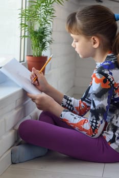 Passionate girl at home paints a landscape sitting on the floor by the window