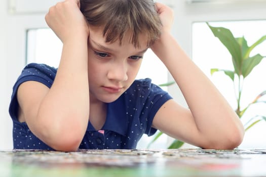 Girl thinking over a puzzle while sitting at home at the table