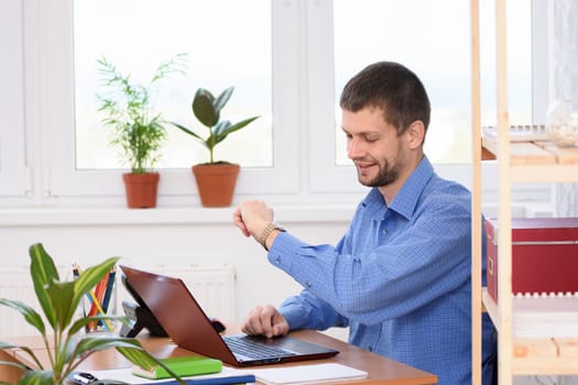 Business man in office looks at wristwatch with smile