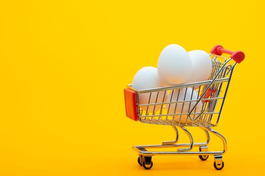 White chicken eggs are in the grocery cart, bright orange background