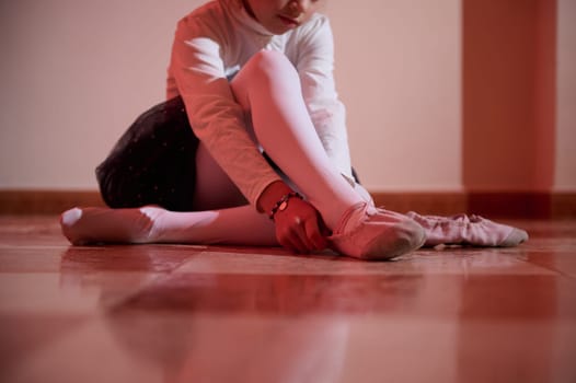 A young ballerina ties ballet shoes, reflecting dedication and grace. The warm lighting enhances the serene atmosphere of the moment.