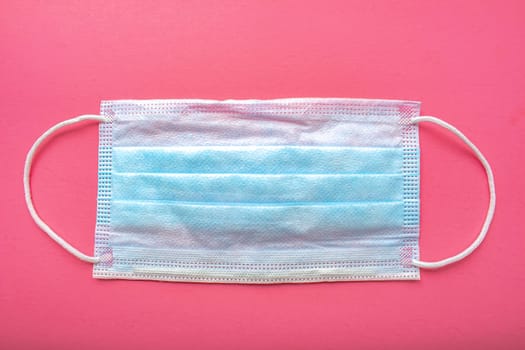 A medical surgical face mask on a pink background