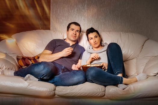 Couple of adults sitting together on sofa and watching movies from comfort of their home during covid 19 or coronavirus pandemics and quarantine