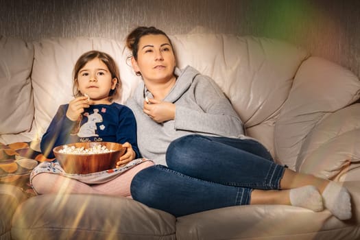 Family sitting together on sofa, eating popcorn and watching movies from comfort of their home during covid 19 or coronavirus pandemics and quarantine