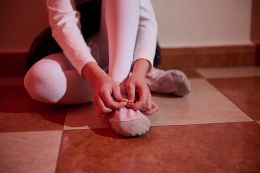 Young ballerina tying shoes, symbolizing preparation, elegance, and focus in a warmly lit space.