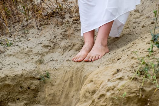 Legs of a girl in a white dress on the edge of a cliff. The sand is falling from the edge of the cliff.