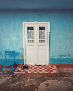 Wooden crutch and a pair of old footwear on threshold, doorstep of a rustic house. Traditional rural building facade in Moldova. Blue lime painted walls and white colored door. Vintage home details.