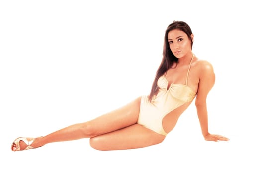 A beautiful young woman in a beige swimsuit sitting in the studio on the.floor with her long black hair, isolated for white background.