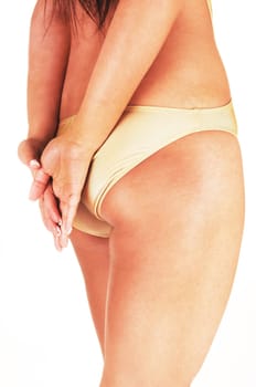 A slim woman standing from the back in a beige swimsuit with her hands.over her bottom, body part, isolated for white background.