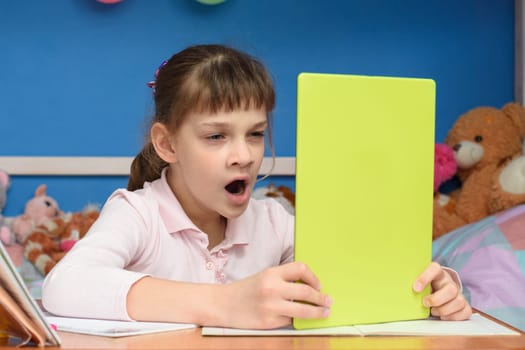 Girl at home at the table yawns while watching a boring video tutorial