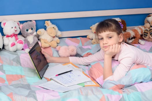 Schoolgirl does homework while lying in bed with a tablet