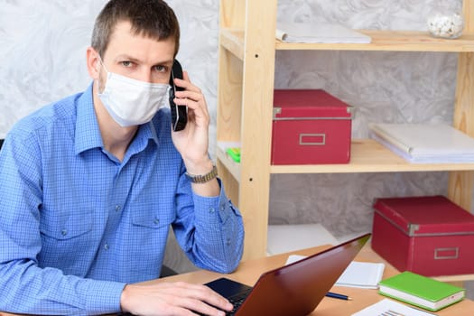 Office specialist in a medical mask works at a computer in the office