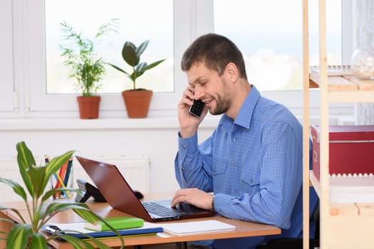 Young businessman talking on the phone in the office and working in a laptop