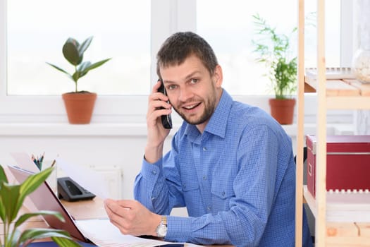 Businessman talking on the phone at his workplace and looking in the frame.