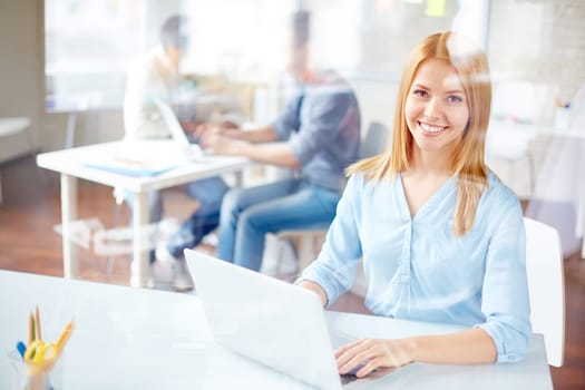Young secretary looking at camera while typing in office