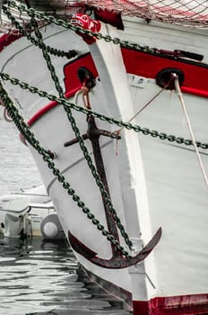 The bow of an old sailing ship with old anchor and neatly painted in red and white.