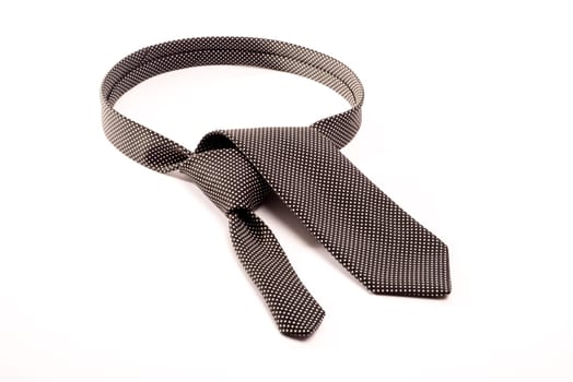 A black tie with white dots on a white background folded as if to make a tie knot around the neck.