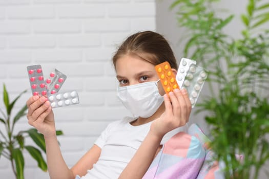 Girl holding in her hands a lot of pills in a pack, even in a medical mask in bed