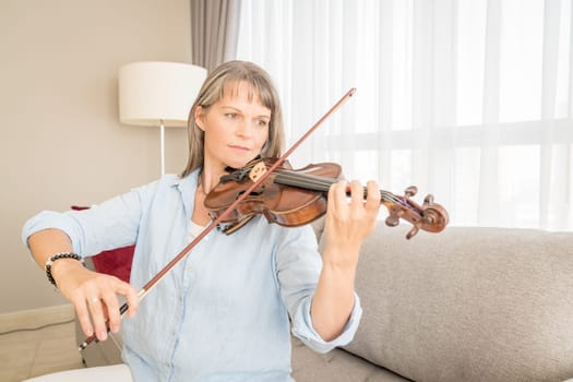 Mature woman playing violin in her urban apartment
