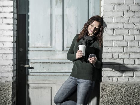 Young woman with red hair using her cellphone and drinking coffee from a takeout cup.