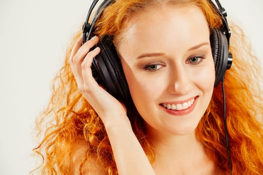 Photo of a beautiful young redhead listening to headphones and smiling.