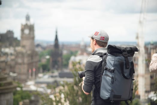 Photographer with backpack and a hat shooting buildings of Edinburgh in a sunny day