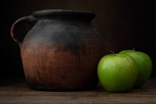 Two granny smith apples with old pottery jug.  Shot at eye level with dark rustic feel.