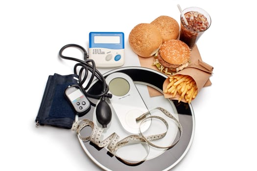 Fast food and medical devices tonometer (blood pressure measuring device) and blood glucose meter, scales and measuring tape on a white background. Concept of unhealthy diet and health.