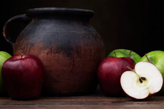 Red adn green apples with old pottery jug.  Shot at eye level with dark rustic feel.
