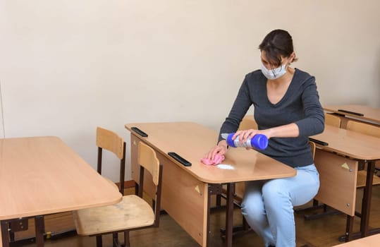 The girl pours cleaning and disinfectant on the desk at the school during the quarantine period