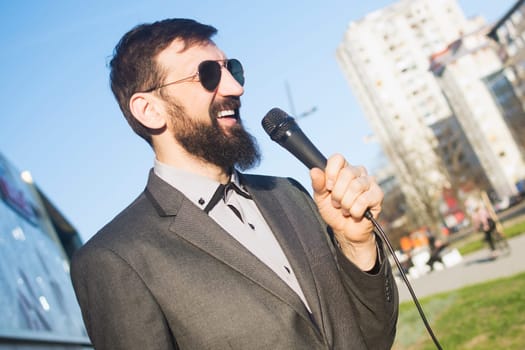 The smiling TV reporter or newscaster is speaking in microphone at the street in live program.