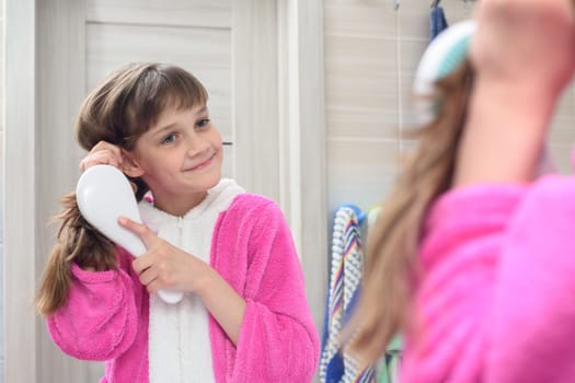 Happy girl combing long hair looks and looks in the mirror