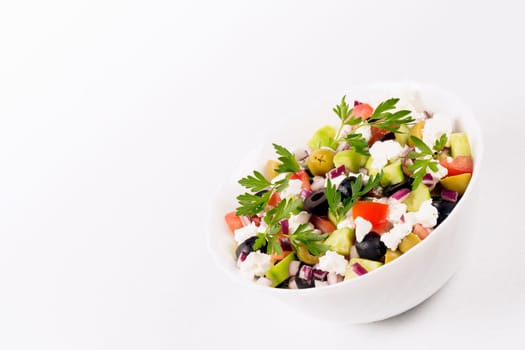 Colorful healthy Greek salad from different vegetables and feta cheese is on white background.