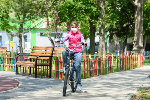 A ten-year-old girl in a medical protective mask rides a Bicycle