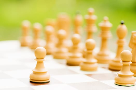 Pawn chess piece and other white chess pieces are on chess board on green background.
