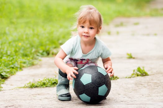 The cute little girl is playing with soccer ball on the street.
