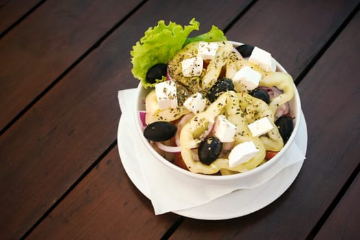 Healthy Greek salad with pepper, olives and feta cheese is on table on brown background.